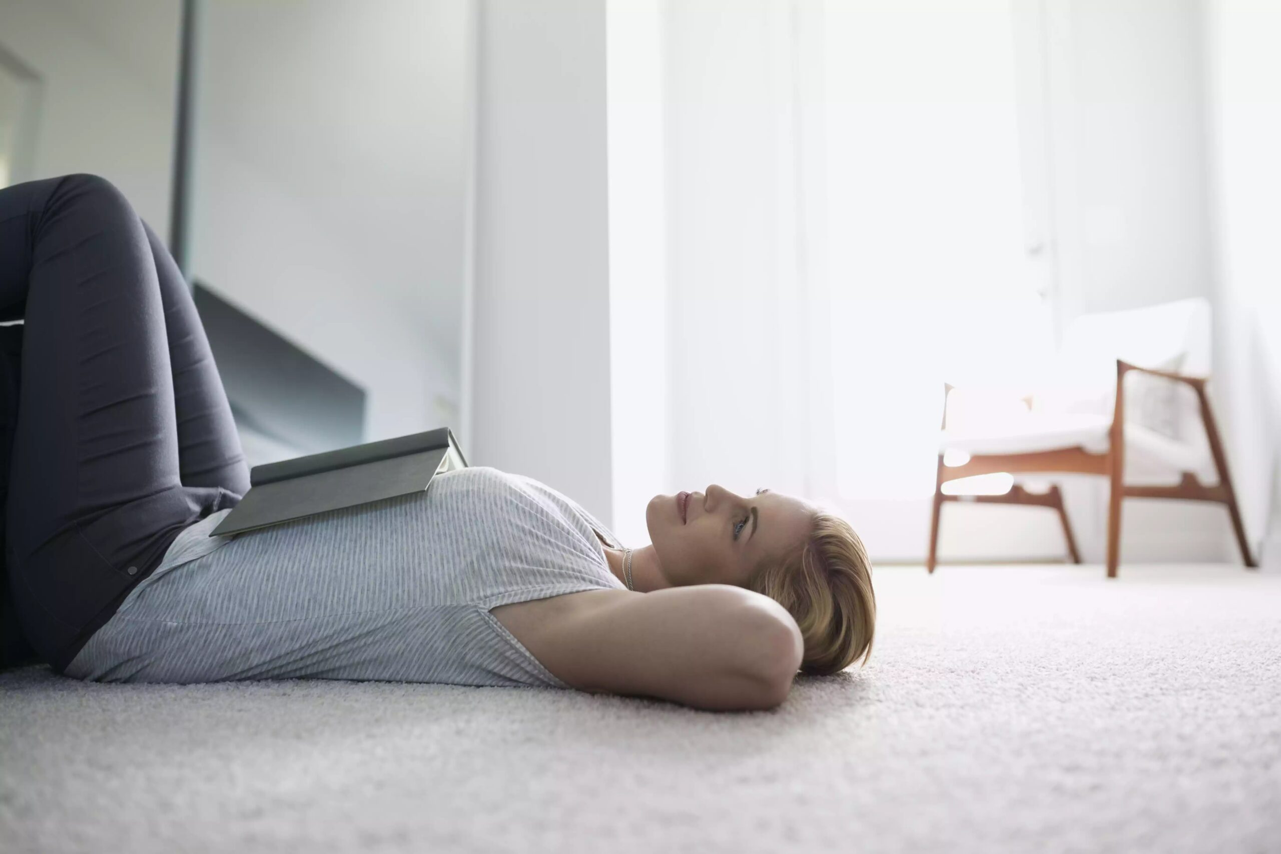 Serene woman with book, laying on bedroom floor