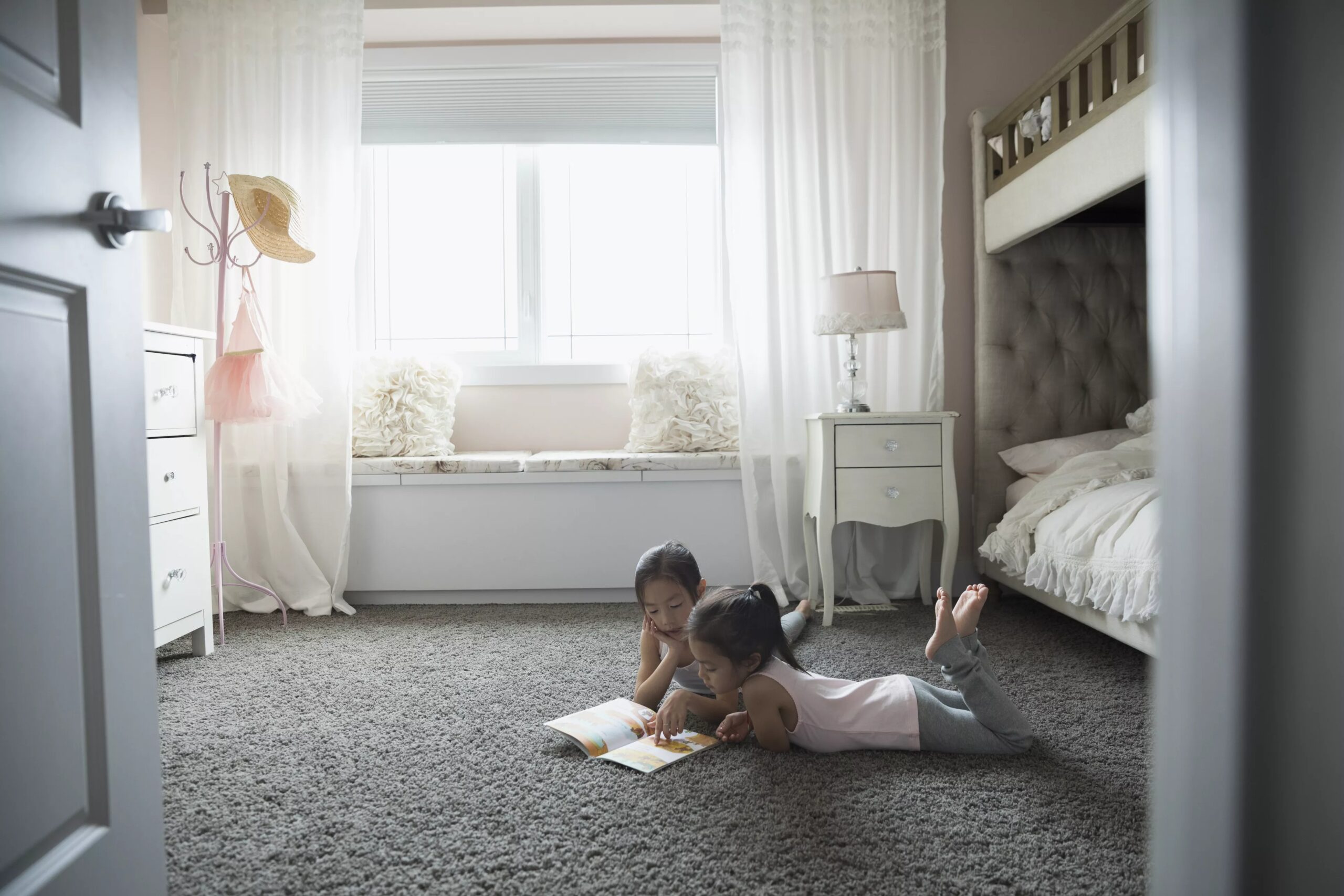 Sisters reading book on carpet in bedroom
